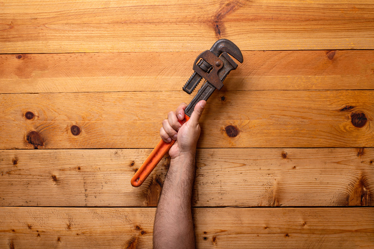 Arm holding pipe wrenches on light wooden background - Labor Day rendition image