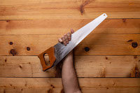 Arm holding woodworking hand saw on light wood background - Labor Day