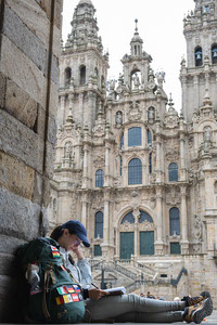 Young woman pilgrim reading a book in front of the cathedral of Santiago de Compostela